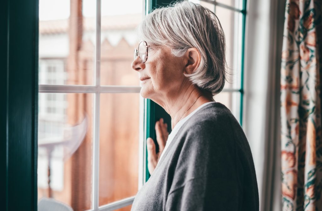 A senior looks forlornly out of their living room window, worrying about their increasing memory loss