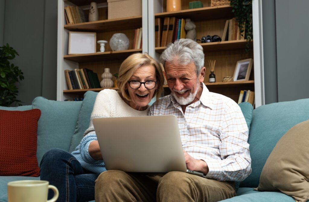 An excited senior couple use a laptop in their living room to research promising assisted living communities